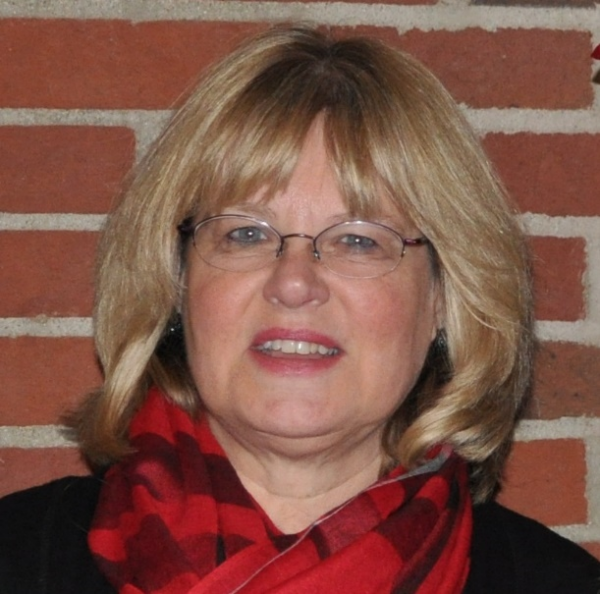 blonde woman with glasses and red scarf with a back drop of a brick wall