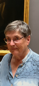 head shot of older woman with grey hair and glasses and blue button up shirt